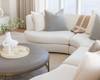 Living room with curved sofa in neutral upholstery and pillows and leather upholstered coffee table