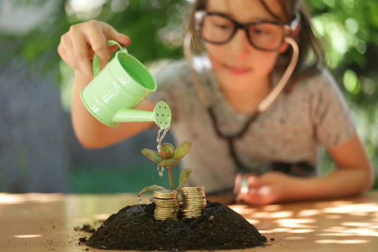 Girl watering a plant which is growing from a stack of coins
