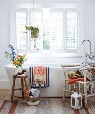 A white bathroom with a large window with shutters and country touches of wood and texture