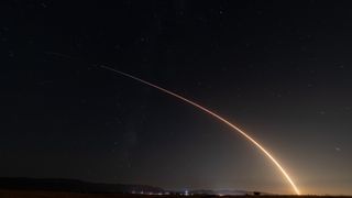 A rocket launch carves an orange arc into a dark night sky in this long-exposure photo.