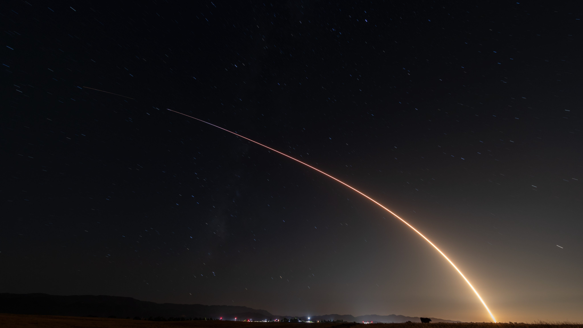 In this long exposure photograph, a rocket launch draws an orange arc across a dark night sky.