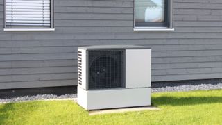 heat pump on concrete slab on lawn with grey timber clad house behind