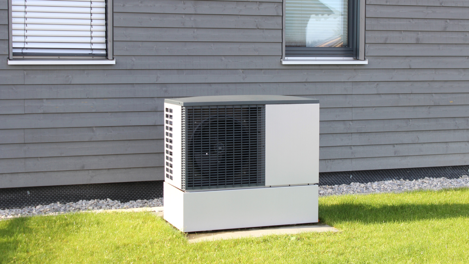 heat pump on concrete slab on lawn with grey timber clad house behind