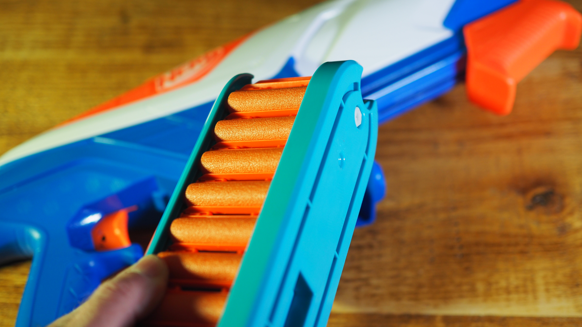 A Nerf N-Series Infinite blaster lying on a wooden table while a hand holds up the ammo clip