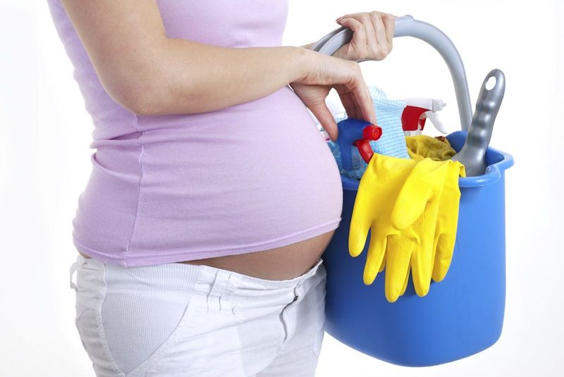 A pregnant woman holds a bucket of cleaning supplies