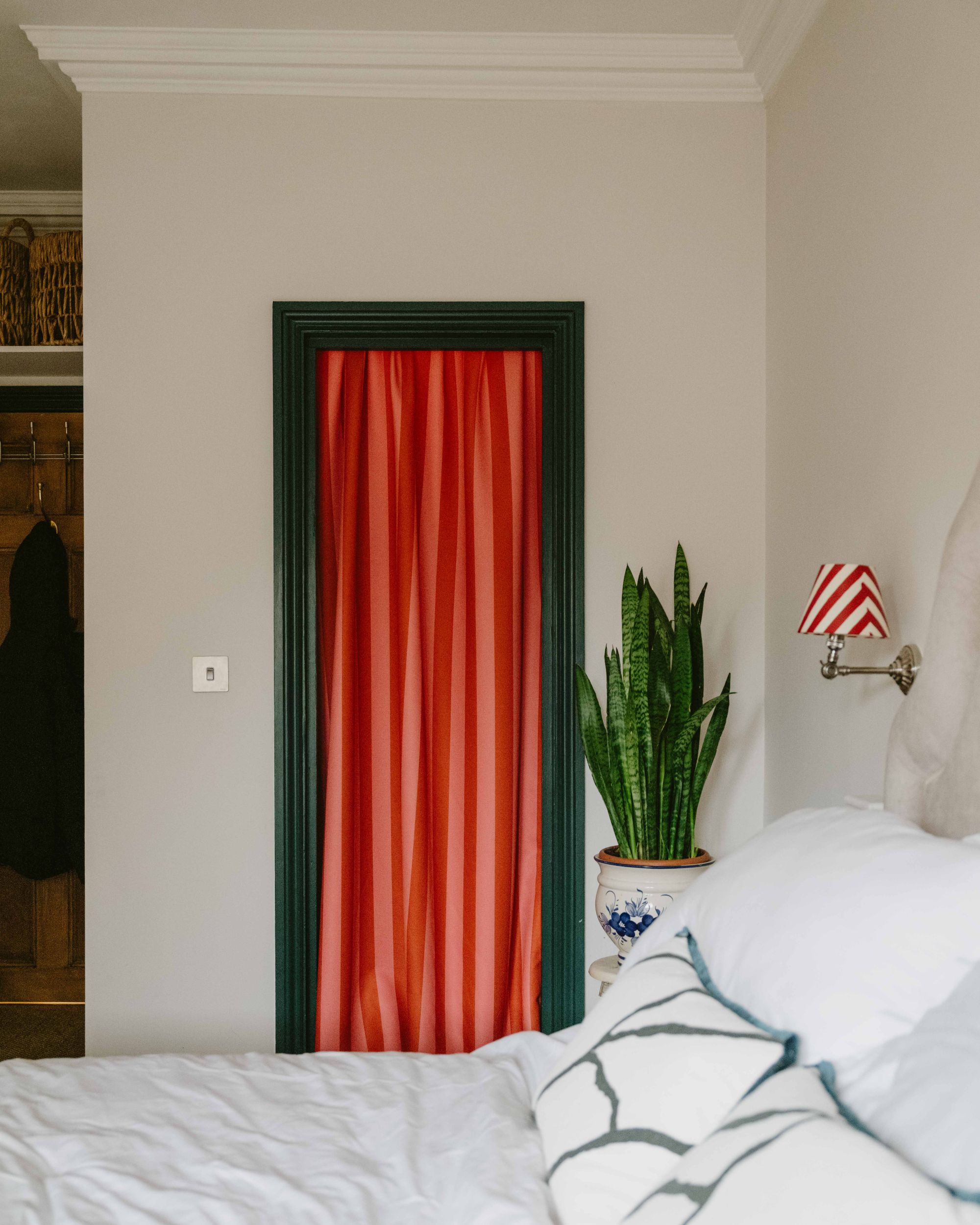 a bedroom with a bright red and pink striped curtain blocking a closet with a green doorframe