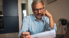 A man looks over paperwork while sitting at his dining room table.