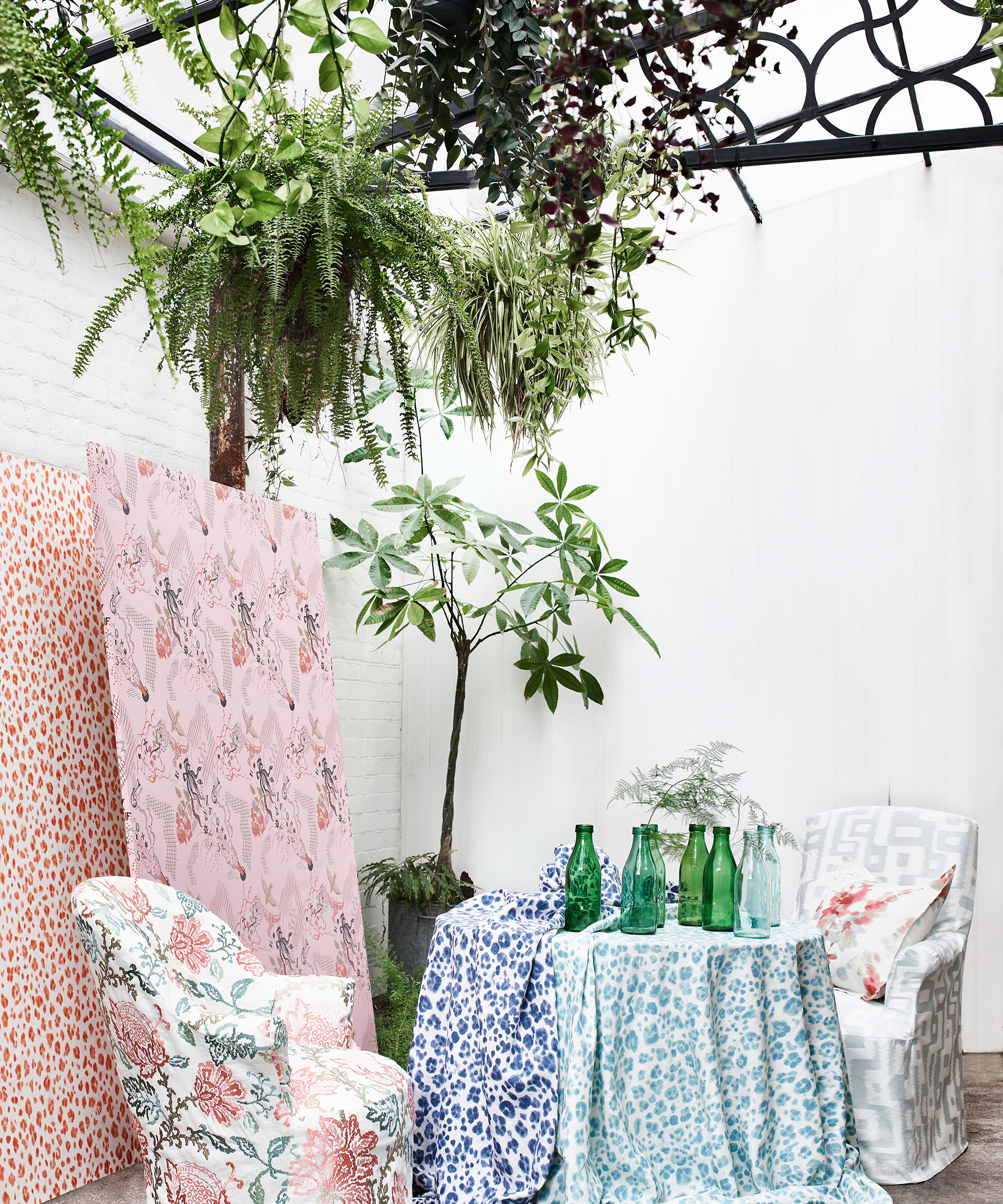 Balcony garden ideas featuring multiple different pastel and floral fabrics draped over a table and chairs, with a potted tree and white walls in the background.