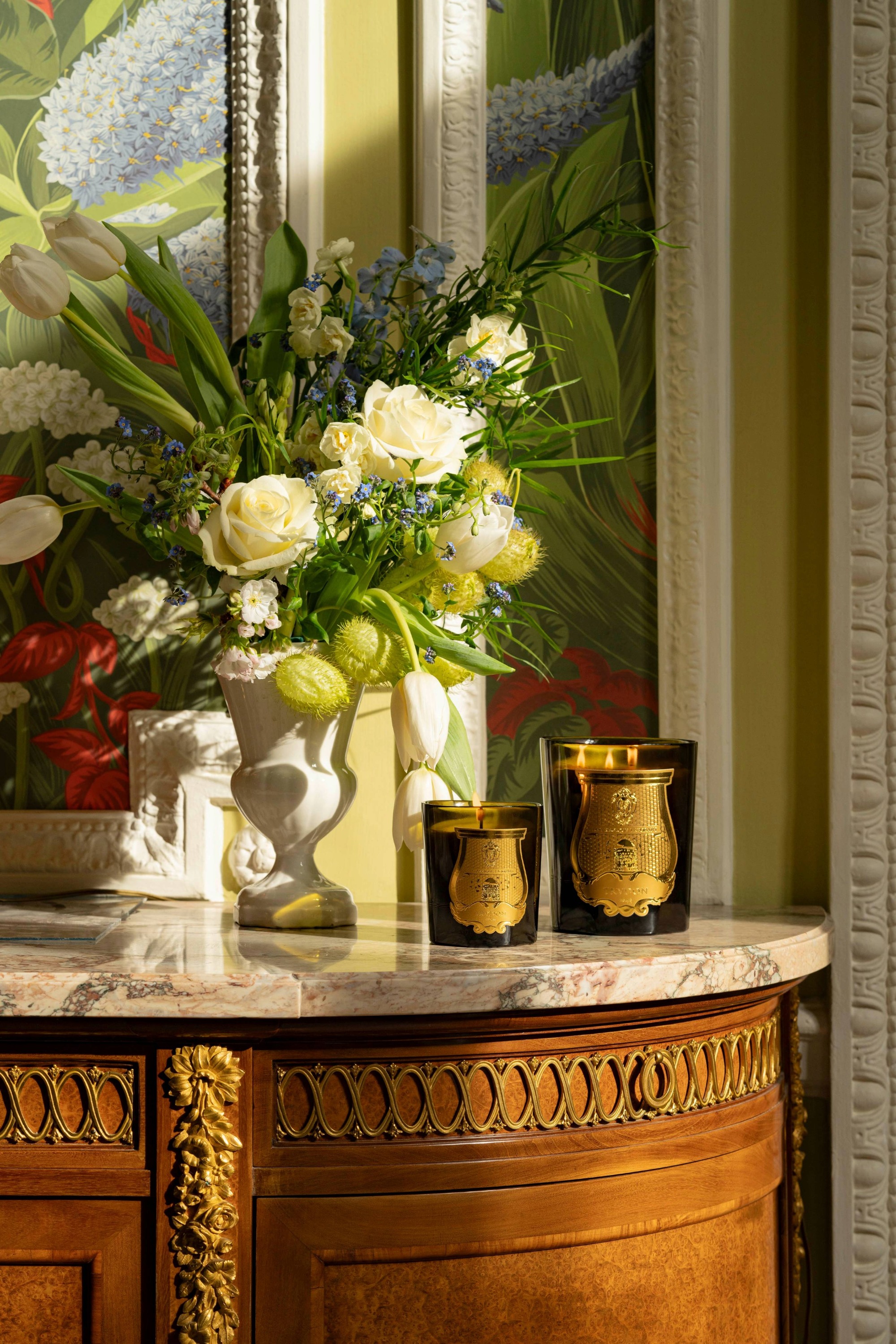 trudon candles next to a floral arrangement on a marble table