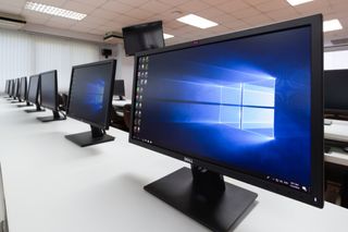 A long office desk with multiple PCs displaying Windows 10 home screen