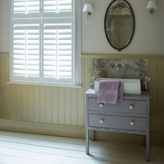 bathroom trends, classic bathroom with tongue and groove in pale yellow, white shutters, vintage mirror, vintage chest of drawers with sink, lilac towel