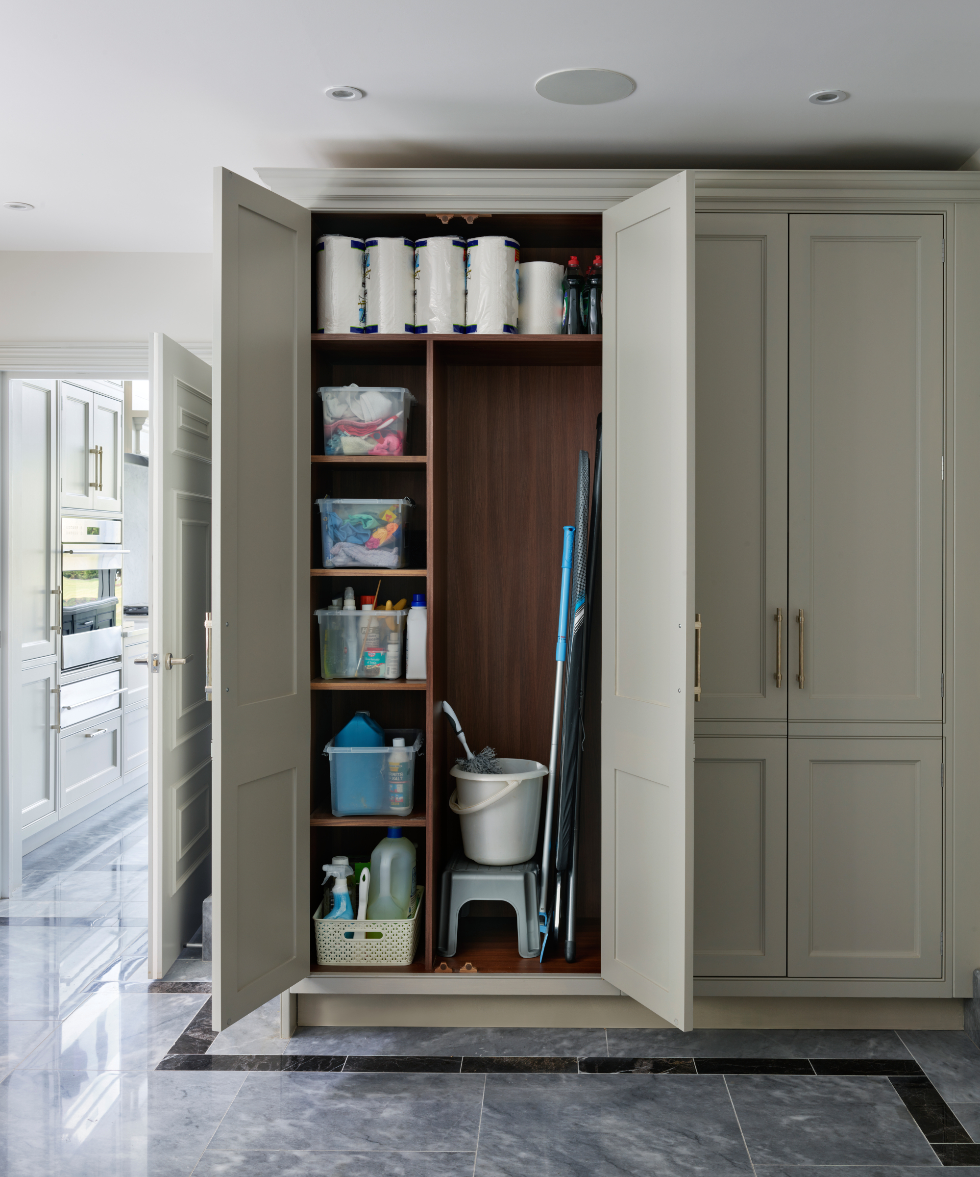 tall cupboards in utility room with shelves inside plus large section containing ironing board, mop, stool and brush