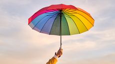 A hand holds up a colorful umbrella an a cloudy day.