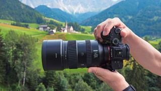 Viltrox AF 135mm F1.8 lens in hand, scenic mountainous backdrop