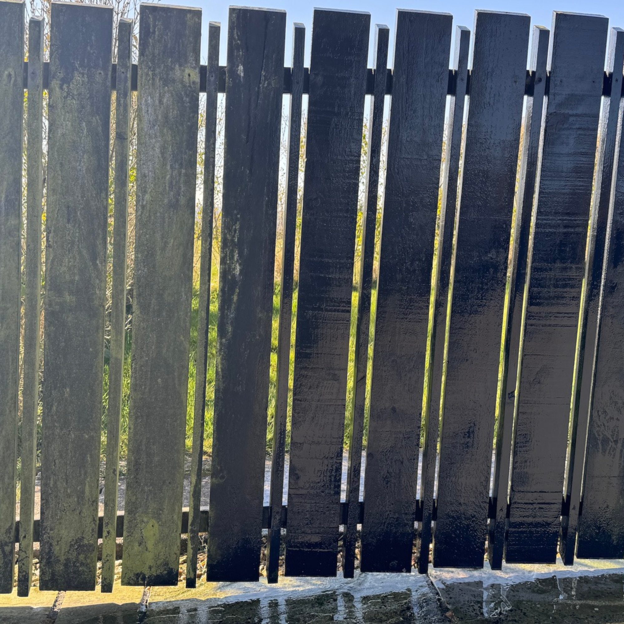a newly cleaned fence beside a dirty fence