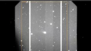 A gray scale image showing various white dots of stars and comets with a large smudge in the middle which is the interstellar comet 3I/ATLAS