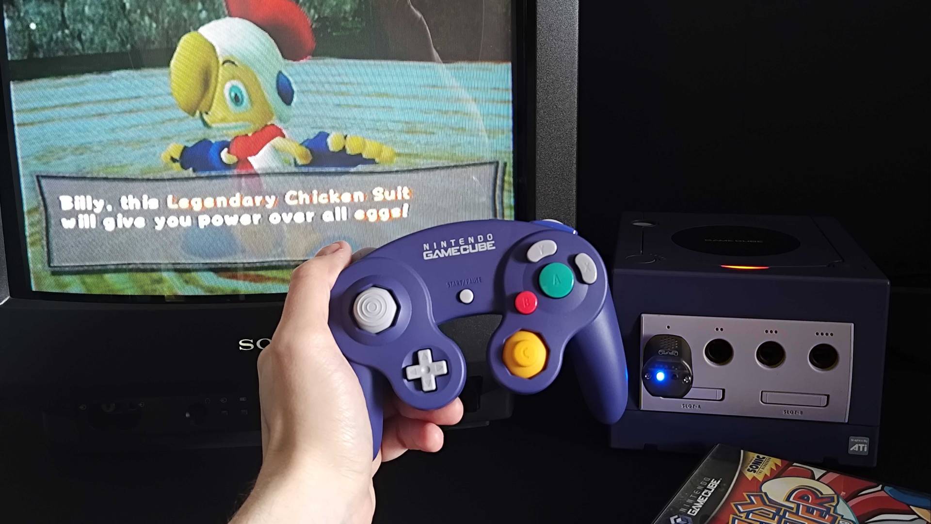 Hand holding Switch 2 GameCube controller with console and CRT in backdrop with Billy Hatcher and the Giant Egg gameplay on screen.