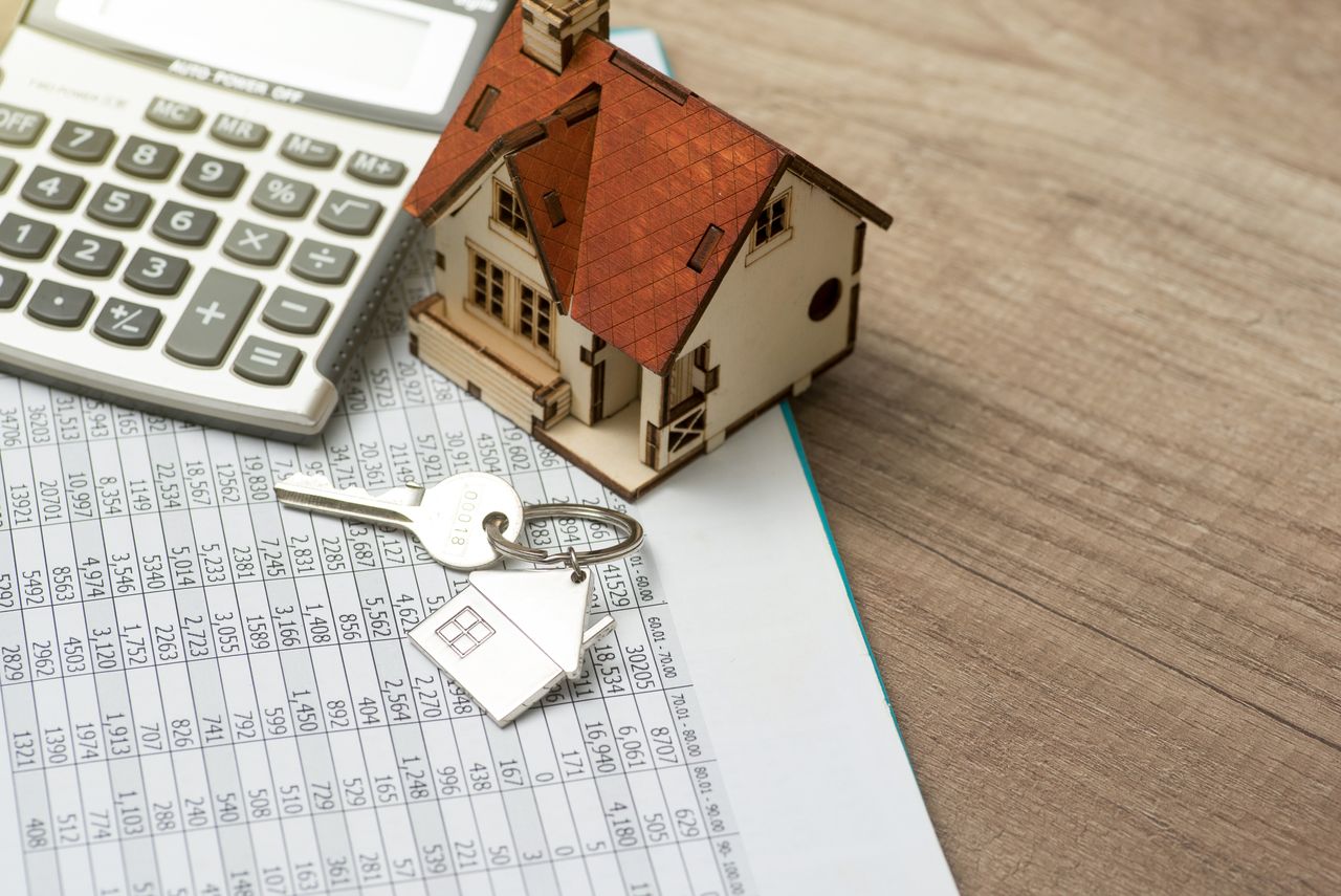 Wooden figure of a house, keys, and calculator on top of a spreadsheet