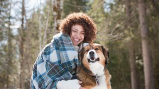 Smiling woman wrapped in a blanket in the forest with her dog
