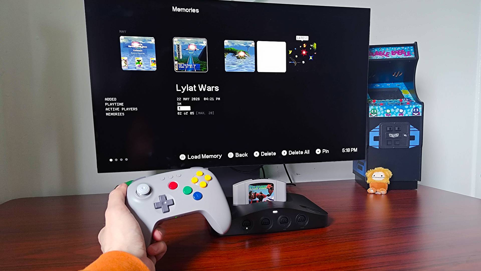 Hand holding 8bitdo N64 controller in gray next to Analogue 3D connected to LG OLED monitor with Star Fox 64 save states displayed.