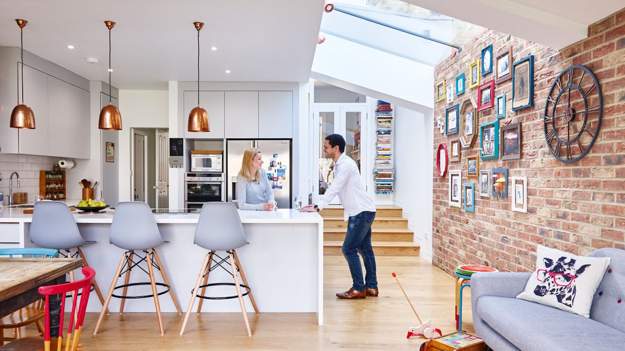 couple in their modern open plan kitchen diner with exposed brick wall