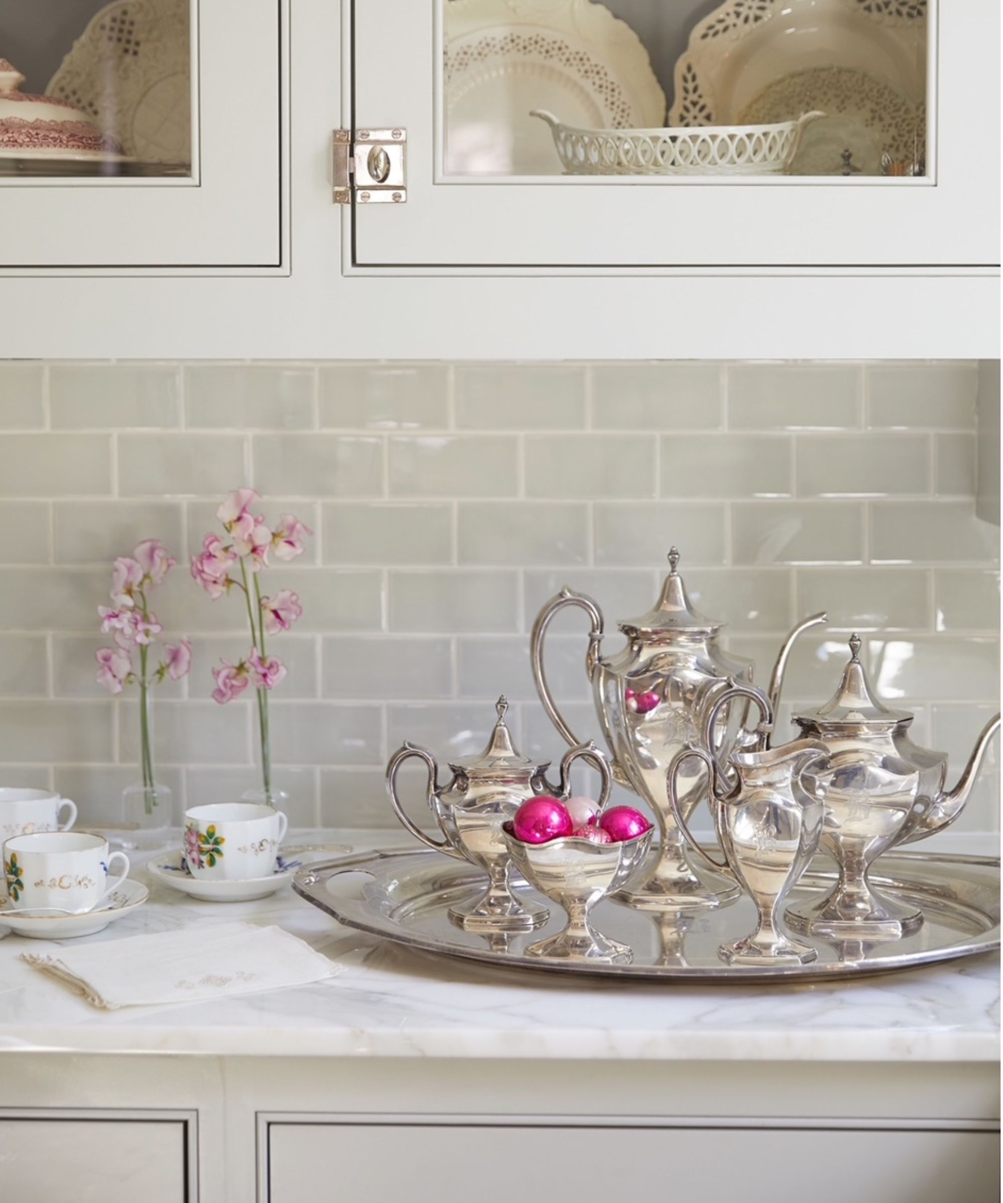 Tray of silverware and pink Christmas ornaments on a kitchen sideboard