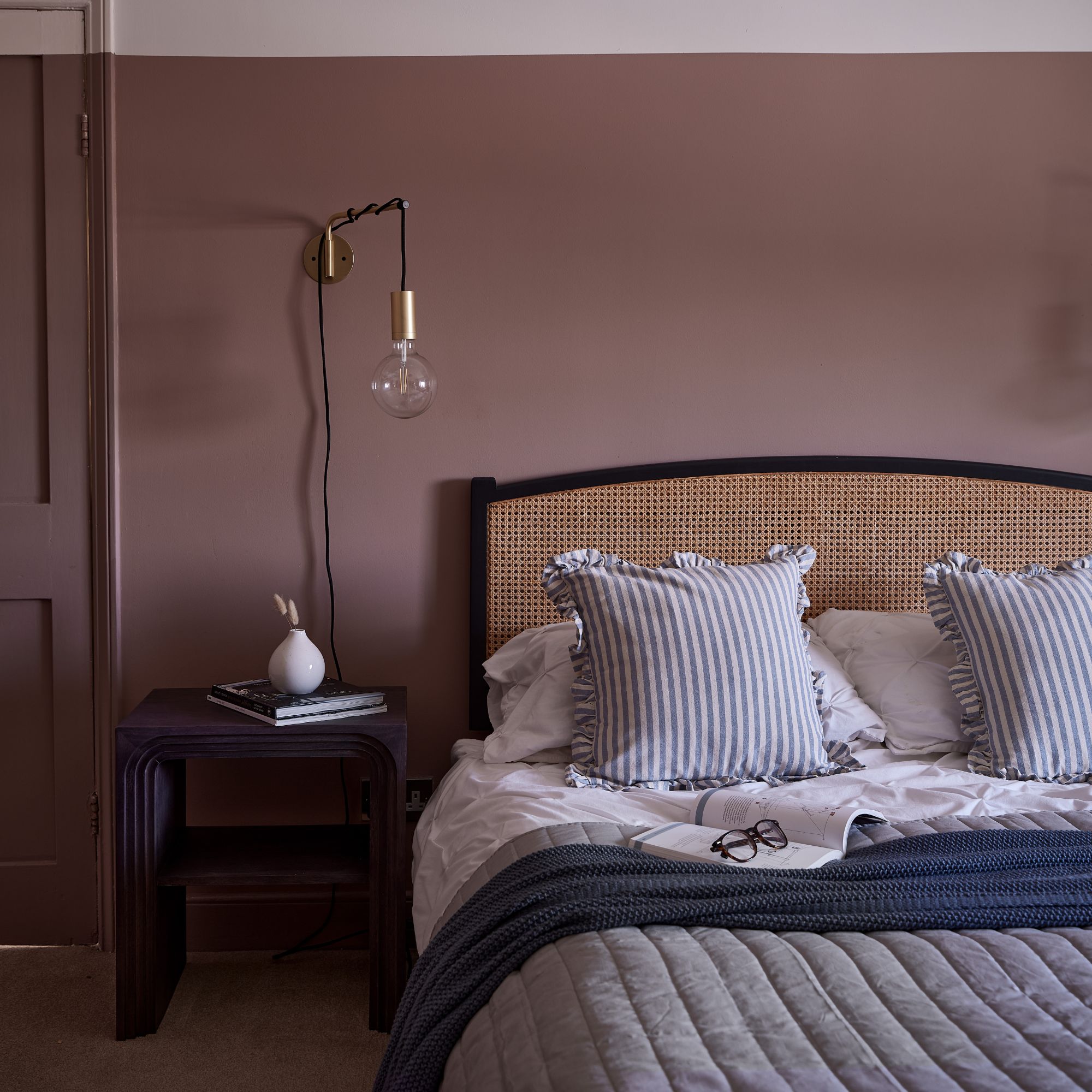 Dark pink bedroom with a rattan bed frame and layered bedding on the bed