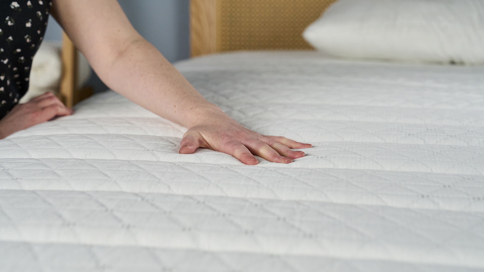A person's hand rests against the surface of the Helix Dawn Mattress, testing the feel and temperature.