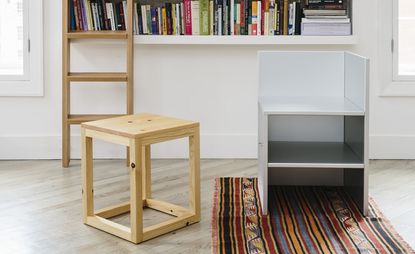 Pine stool next to a white shelf placed on a colourful rug. Behind is a book wall shelf with windows on both sides