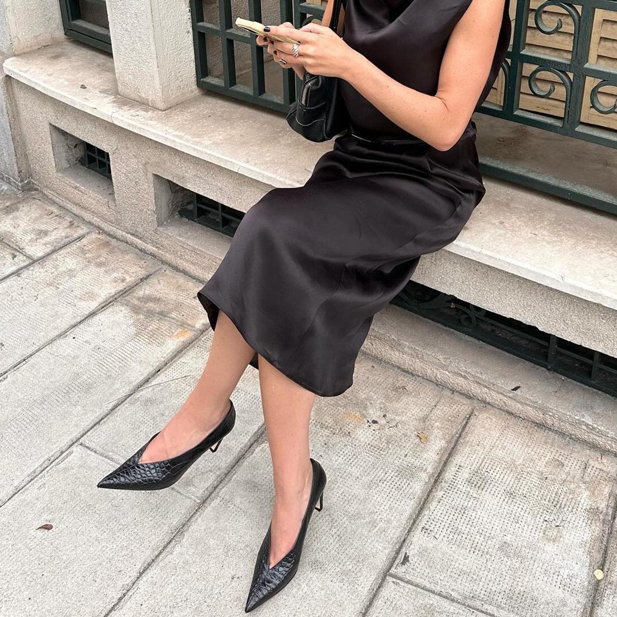 Woman looking at her phone wearing a black satin dress and pumps