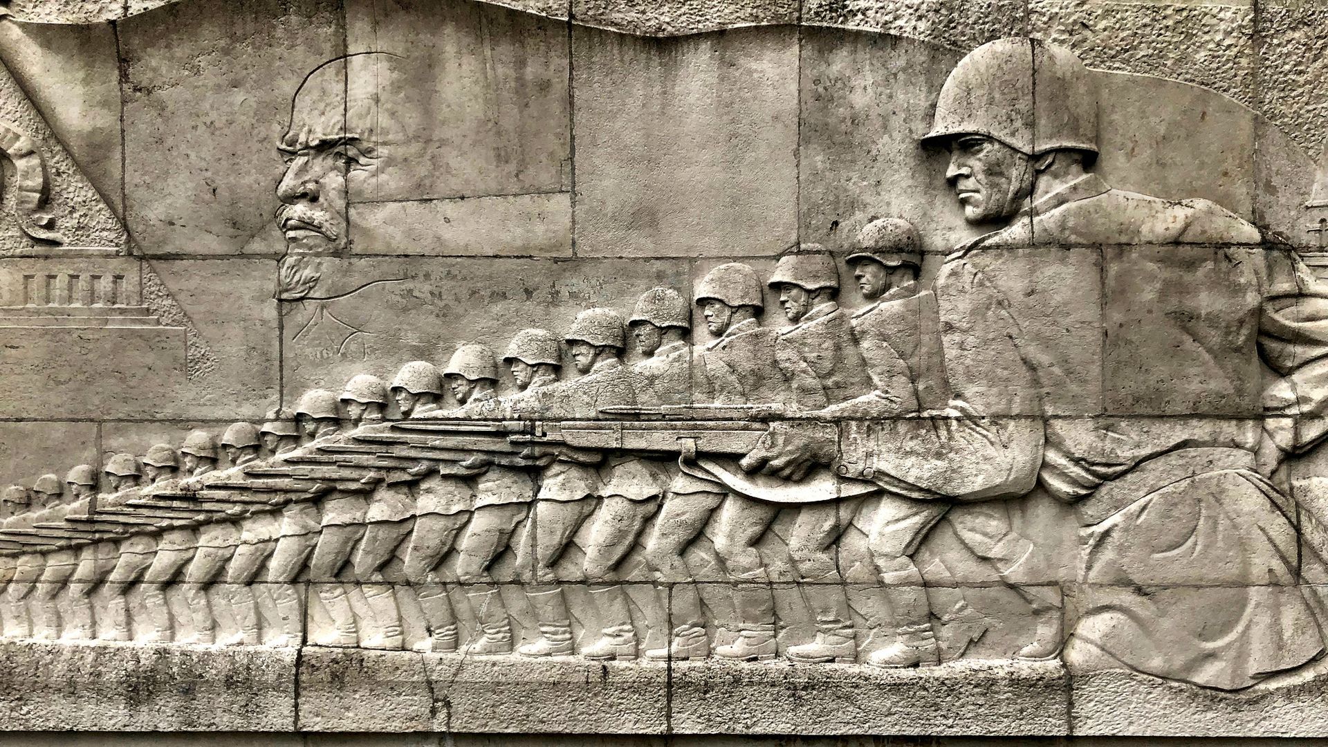 A wall carving of soldiers with circular helmets carrying guns