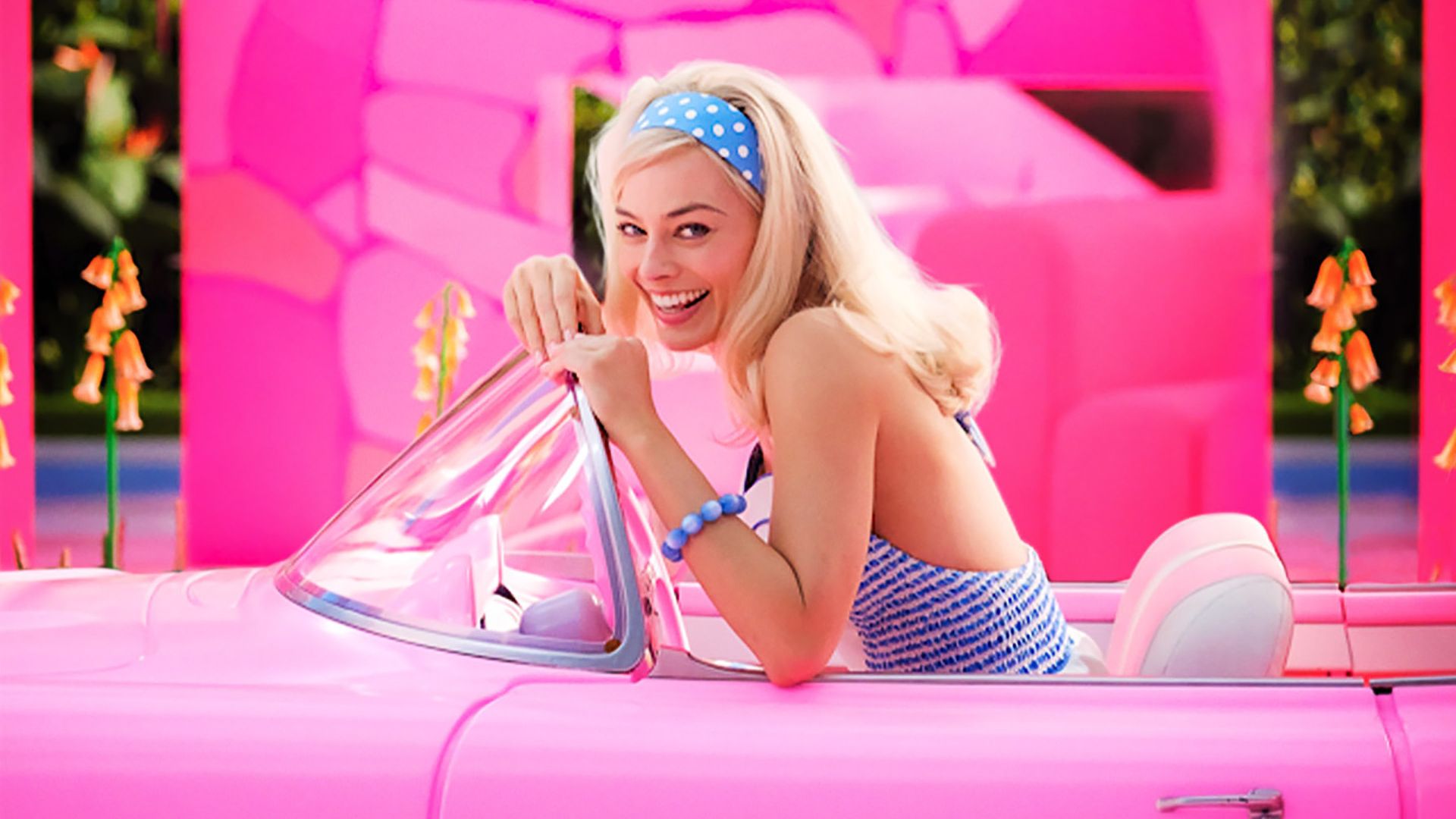 Margot Robbie's Barbie smiles as she sits in her pink car in her solo movie