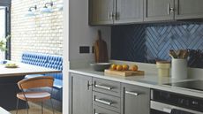 Close up of kitchen counter with blue tiled backsplash, dark wooden cupboards, banquette seating in background