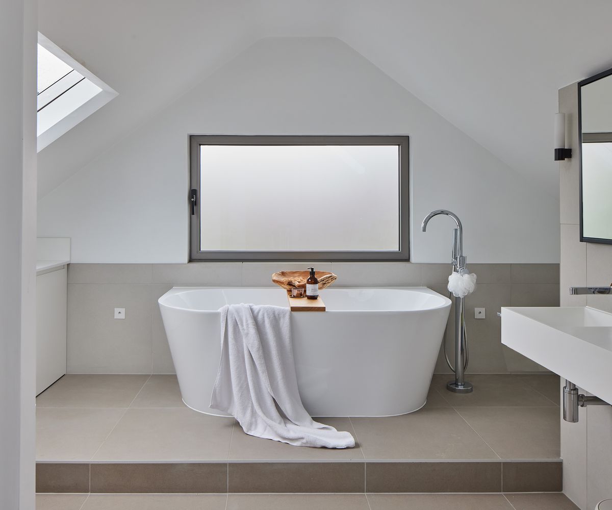 A freestanding tub with frosted glass window and grey floor tiles