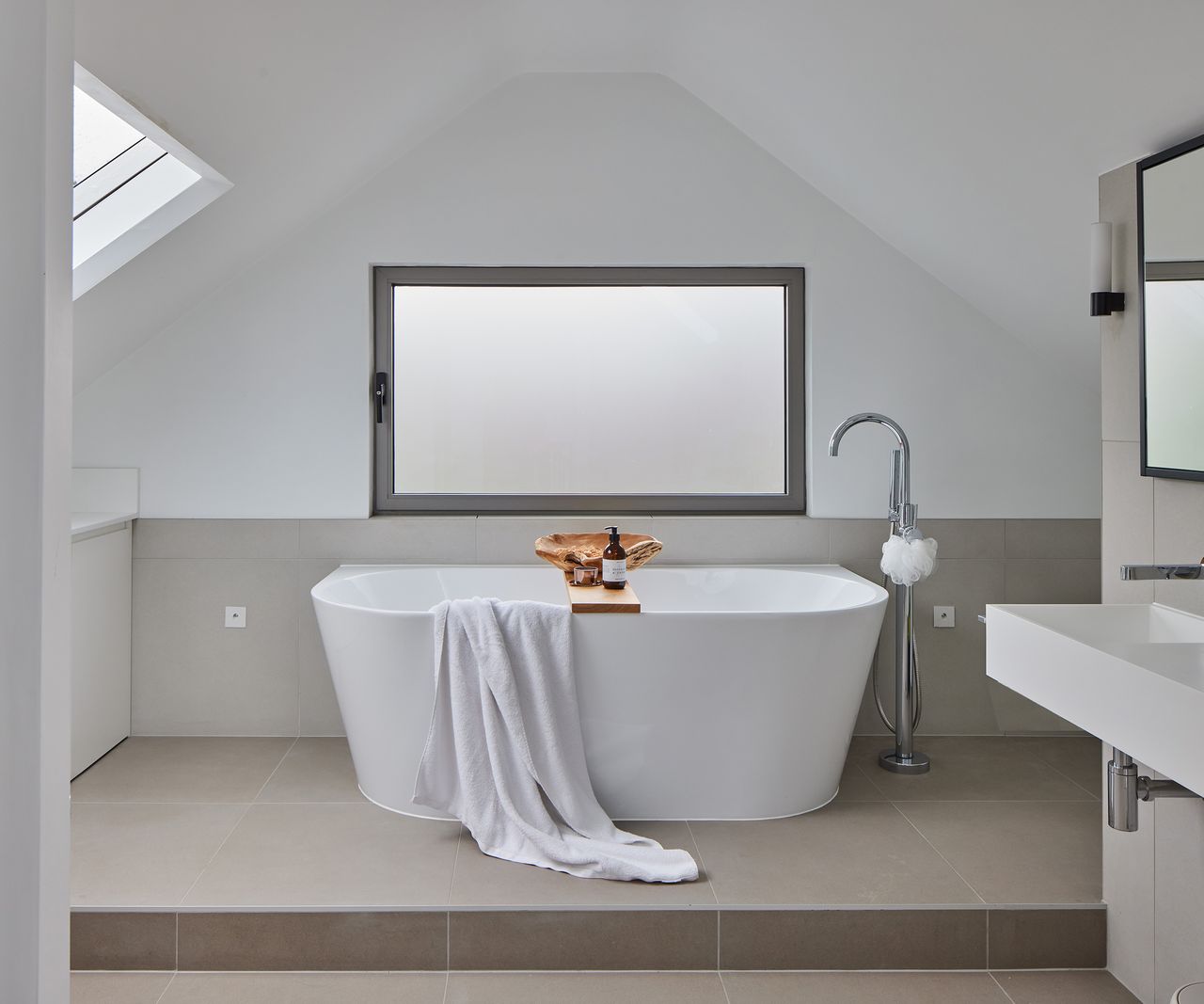 A freestanding tub with frosted glass window and grey floor tiles