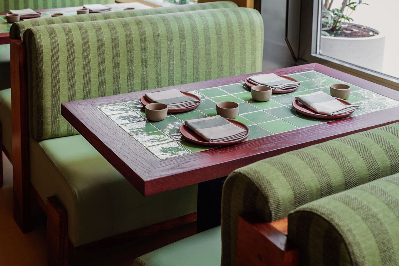 Minty green fabric and wood banquettes turn tiled water green tables into intimate dining booths adorned with red clay plates, organic ceramic bowls, and stripy napkins.