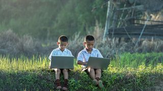 Two children outdoors using laptops.