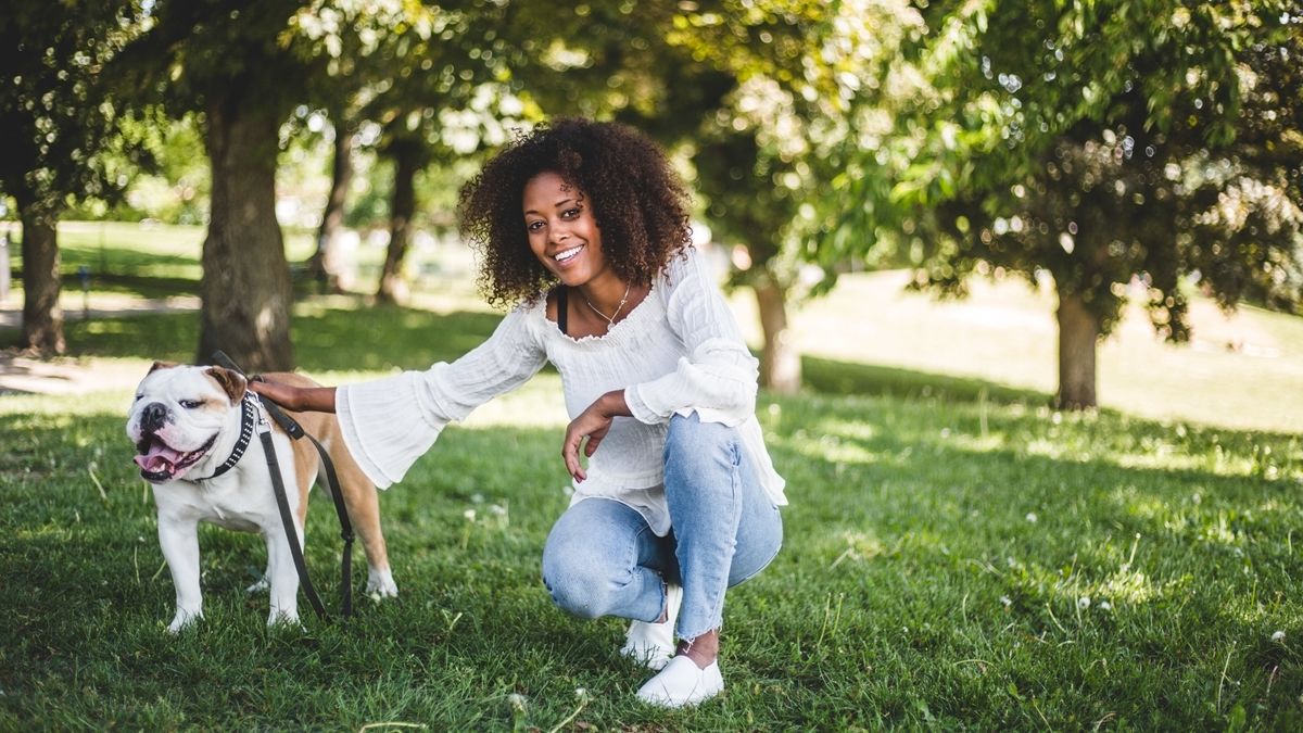 Portrait of smiling woman with bulldog on grassy field at park