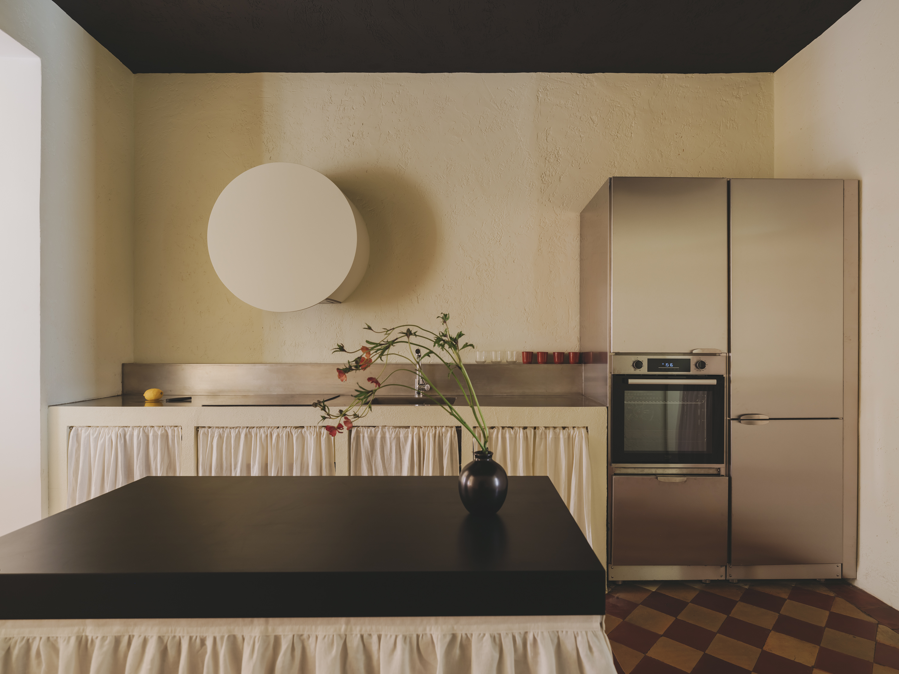 The kitchen, mixing stainless steel, plastered walls, and draped cabinet covers.