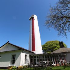 lighthouse in red and white colour near house with sloping roof top