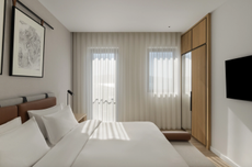 A sleek modern hotel bedroom with large sash curtains in front of the balcony door and window, with the bed in front.