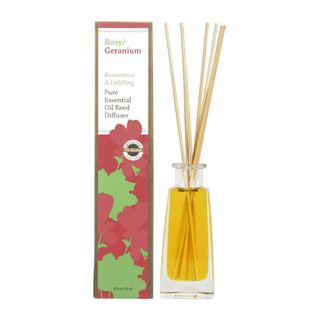 A geranium reed diffuser with wooden reeds next to red and green cardboard packaging box