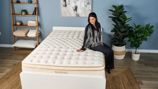 A tester sits on the edge of the bet fiberglass-free mattress, the Saatva Classic