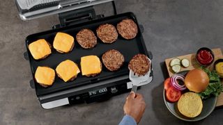 Person cooking 10 burgers using Ninja Sizzle Pro XL indoor grill