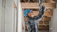 A man in a blue hard hat working on wiring in a roof void