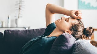 Woman holding fist against forehead, lying down on sofa, representing emotional burnout