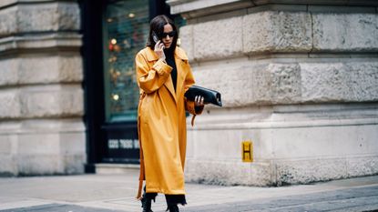 A woman in a yellow coat walks down the road on the phone at London fashion week