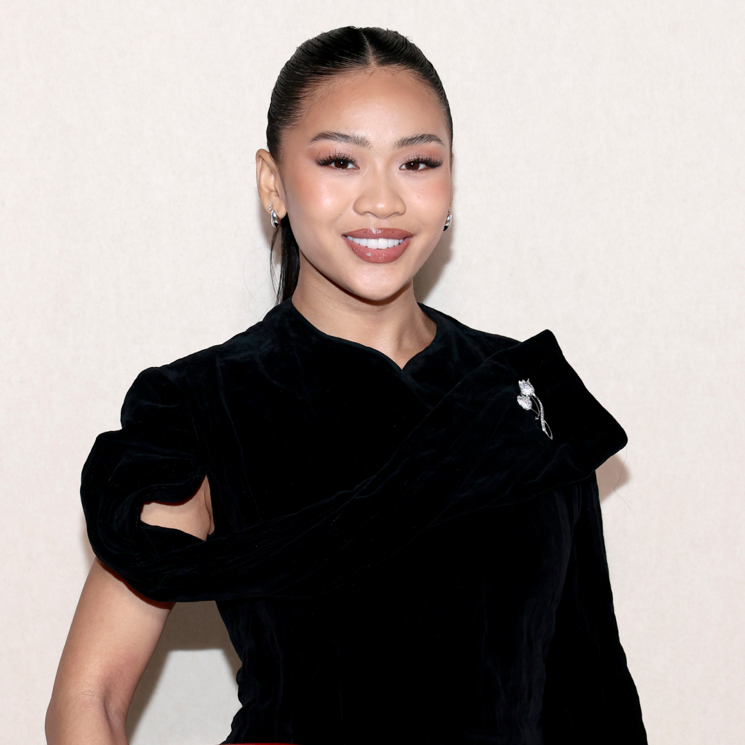 Gymnast Suni Lee wearing a ponytail hairstyle, soft skinlike makeup and a black top. She is smiling at the camera