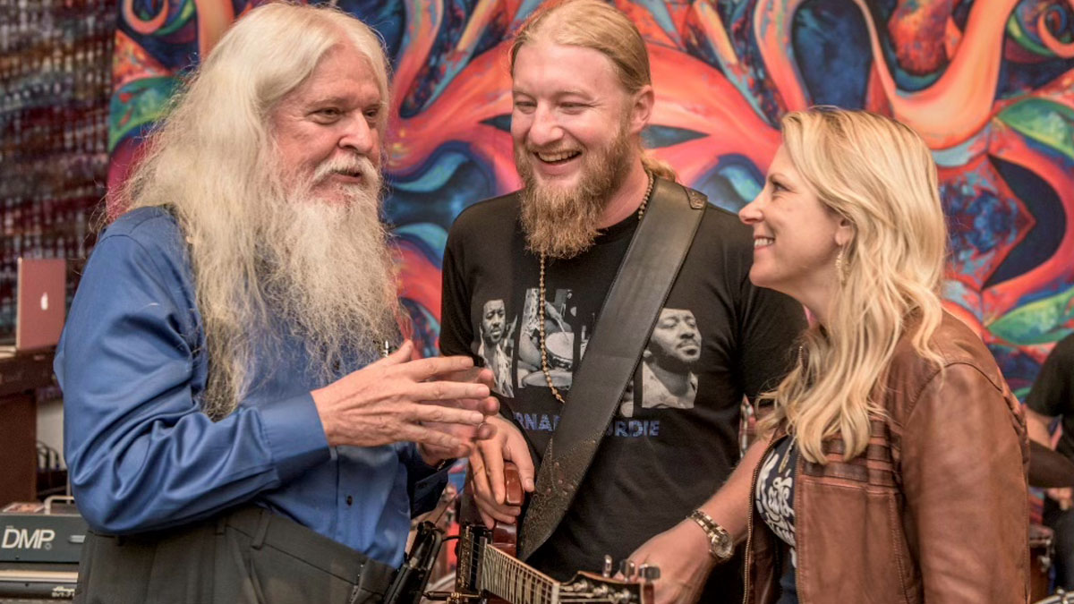 Tedeschi Trucks Band and Leon Russell pictured in front of a brightly patterned wall, with Derek Trucks [centre] holding a Gibson SG.