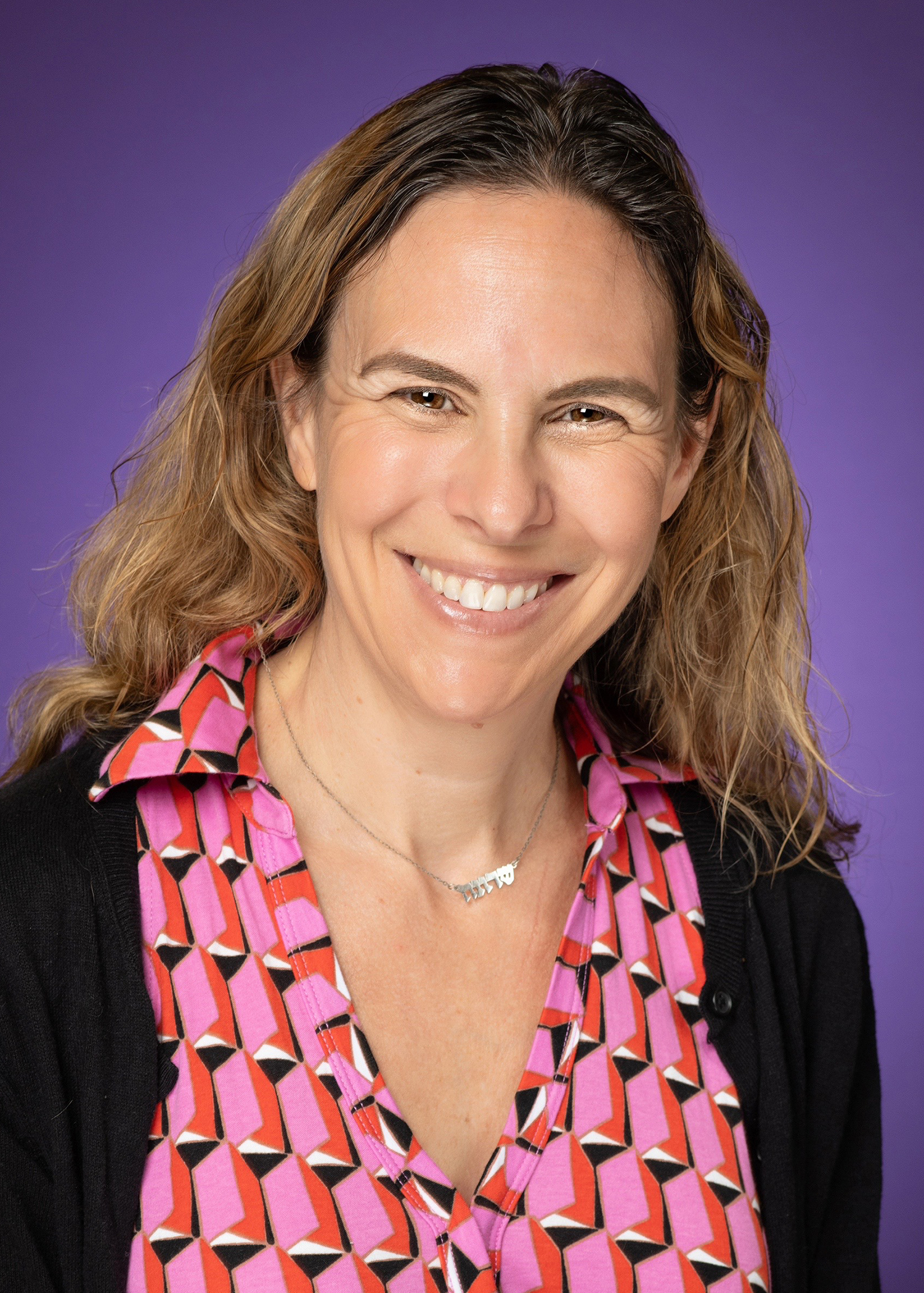 a white woman with dark blonde hair in a pink shirt and black cardigan
